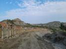 Wooden wall sits against a dirt road that winds through a hilly landscape. Construction materials sit on the other side of the wall.