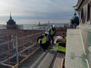Construction workers repair concrete building exterior with body of water and Statue of Liberty in the background