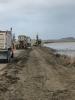 Construction vehicles sit alongside levee leading to a body of water.