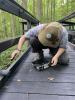 Conservation corps member paints a dark brown, wooden boardwalk