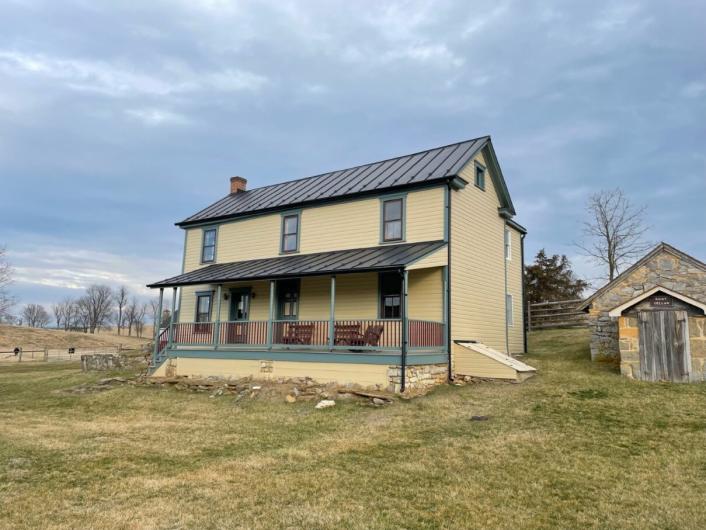 Yellow house with green trim and new roof on a grass lawn.