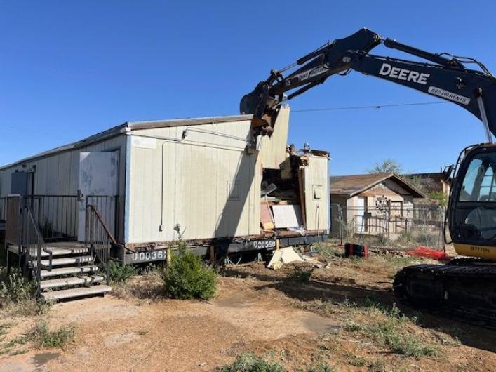 Excavator demolishes a building on a dirt plot at Hotevilla-Bacavi Community School.