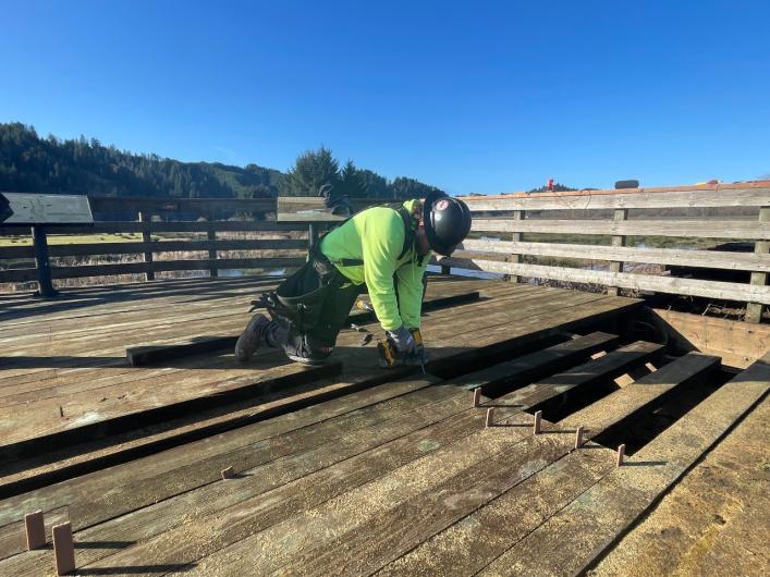 A construction worker removes a deteriorated wooden board on an observation deck.