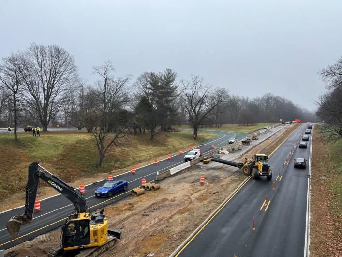 Construction vehicles sit on dirt median with paved roads on both sides.