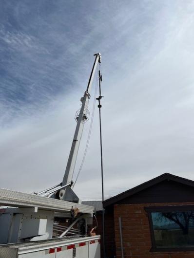 Crane supporting well water inspection next to a brick building.