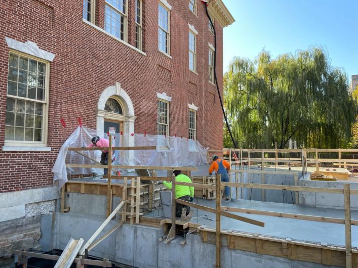 Construction workers stand on concrete platform with wooden railings to repair the exterior of the First Bank.