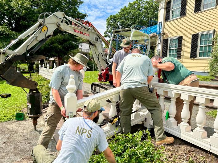 Five workers install a white wooden railing