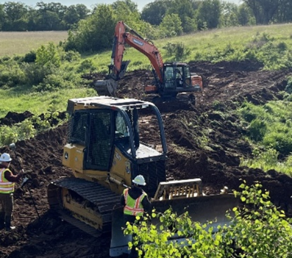 Construction vehicles in construction area surrounded by green field