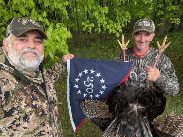 Two hunters with a turkey holding the commemorative flag