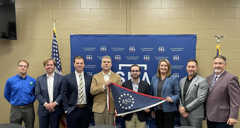 Group of people holding 250 flag in front of blue SBA sign. 