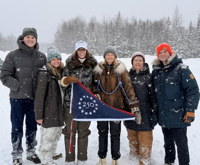 Group of people in snowy weather holding commemorative flag