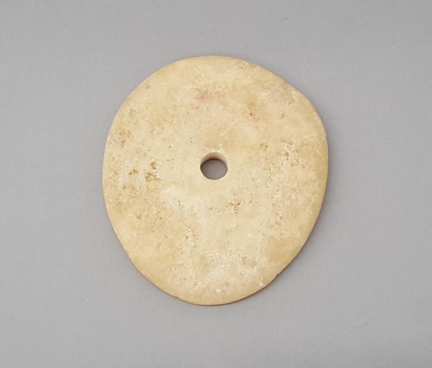 Flat, thin, and circular stone with a small hole in the middle.
