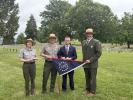 4 people in front of cemetery holding commemorative flag