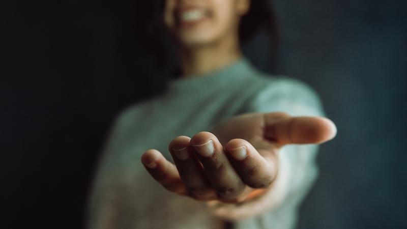 A smiling woman extends her hand in a gesture of support. Photo by Ave through Adobe Stock.