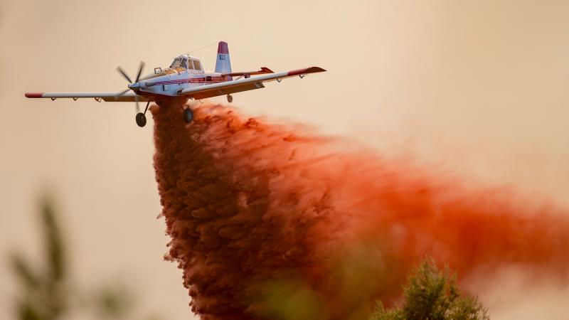 A single engine air tanker drops red-colored retardant on a wildfire.