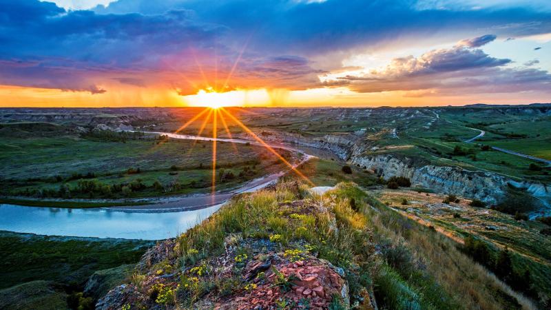 Sunrise over rugged prairie with a river winding through the landscape and flowers blooming