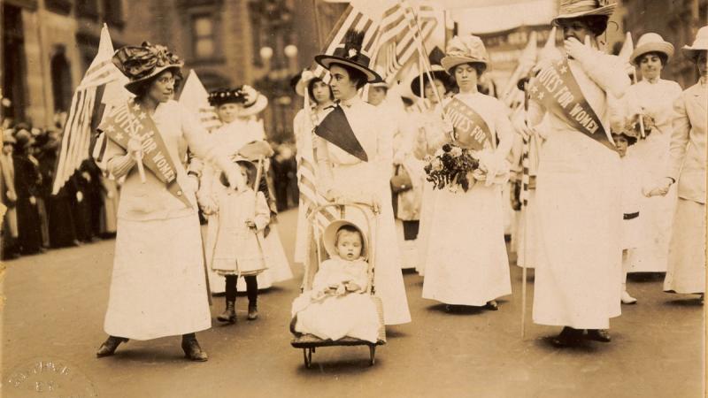 Historical photograph of women marching down a busy street in support of suffrage.