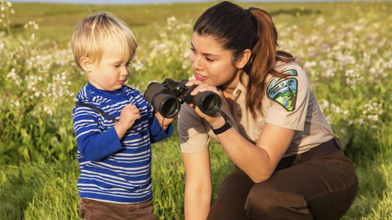 A BLM ranger helps a child look through binoculars