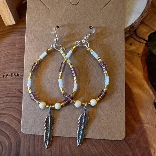 A pair of white, gold, and pink beaded earrings with a feather charm.