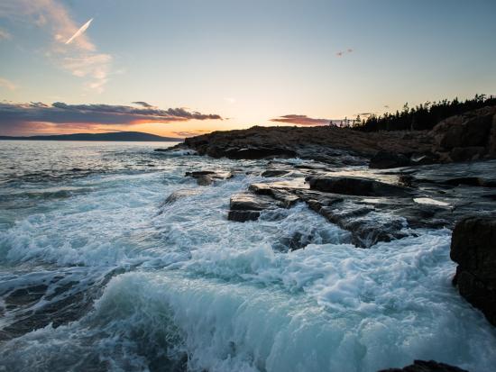 Waves crashing over a rocky coastline at sunset.