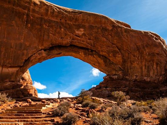 A person stands at a distance under a massive rock arch.