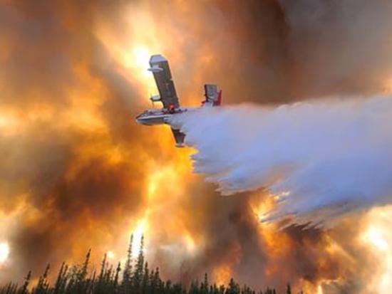 A plane seen from below dropping water on the Clear Fire in Fairbanks, Alaska, against an orange, smoke-filled sky. Photo by Eric Kiehn, Kittitas County Fire District 1.