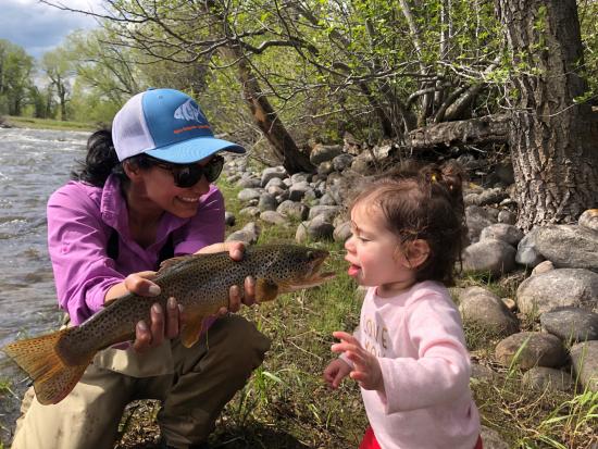 Karen shows her toddler a freshly caught trout along a river bank