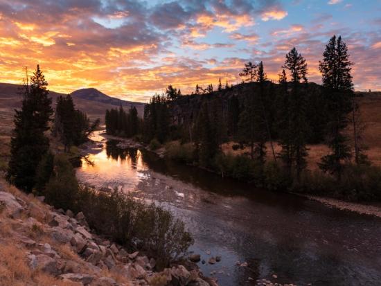 Cloudy sunrise over winding river and mountain peak.