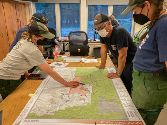 Wildland fire resource advisors study a map showing the outline of a wildfire and the surrounding area during a briefing. Photo by Cedar Drake, NPS.