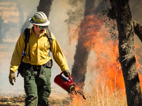 A wildland firefighter with the U.S. Fish and Wildlife Service helps private landowners adjacent to the Balcones Canyonlands National Wildlife Refuge set a prescribed fire to manage vegetation and reduce the risk of an extreme wildfire. He holds a drip to