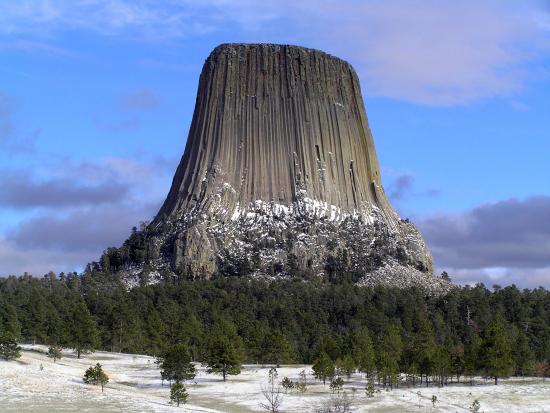A large natural rock tower with vertical groves rises above a hill covered in trees.