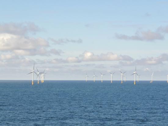 A line of ocean wind turbines against the sky.