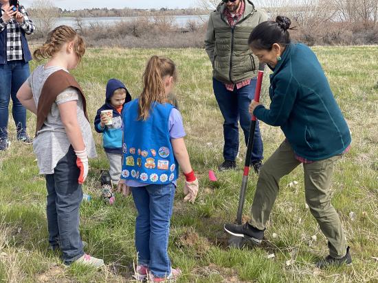 Secretary Haaland and 3 children digging a hole for a plant.