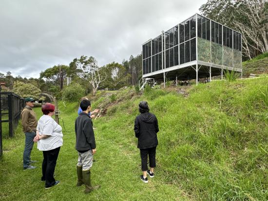 Assistant Secretary Cantor and group of people looking at rectangular bird structure surrounded by vegetation. 