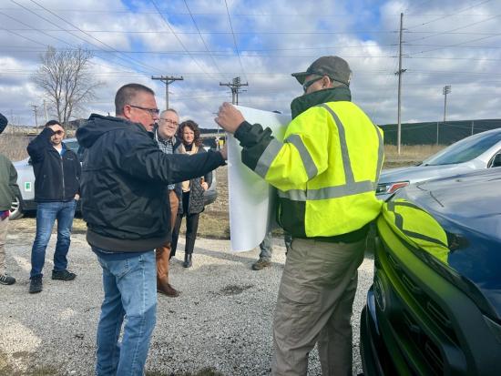 Group of people looking at a poster being held by someone in a safety jacket