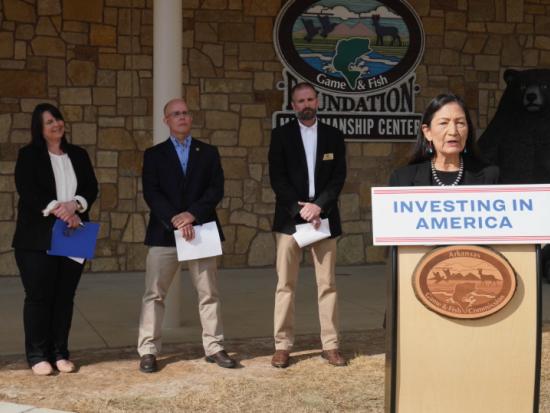 Secretary Haaland standing behind a podium with the sign Investing in America during a visit to Arkansas 