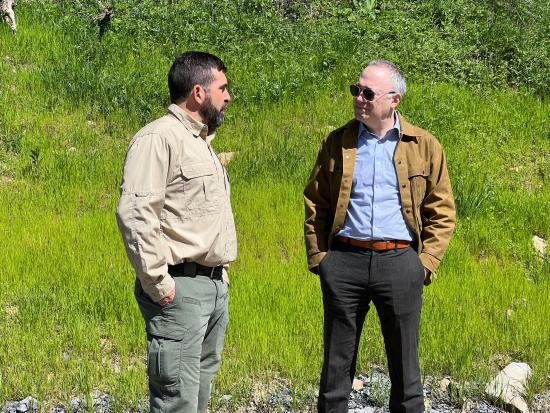 Two men standing in green grassy area talking. 