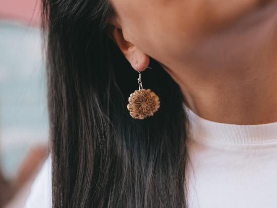 Photograph of a carved antler earring hanging from a woman's ear.