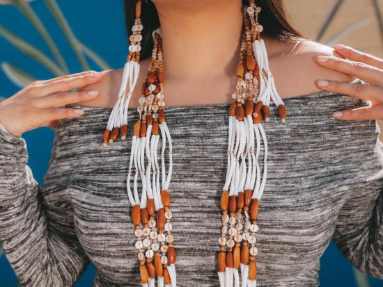 Photograph of woman wearing a set of brown and white dentalium shell necklace and earrings. 