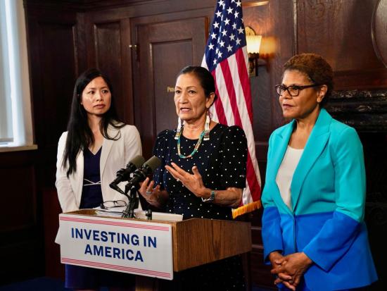 Secretary Haaland and two others stand behind podium