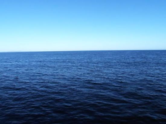 An aerial view of a placid deep blue ocean under a blue sky