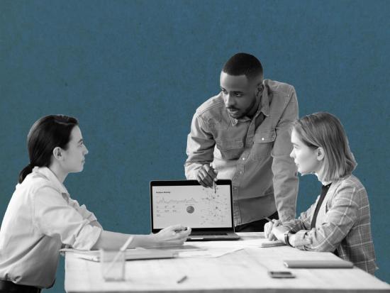 Three people at a desk looking at a computer.