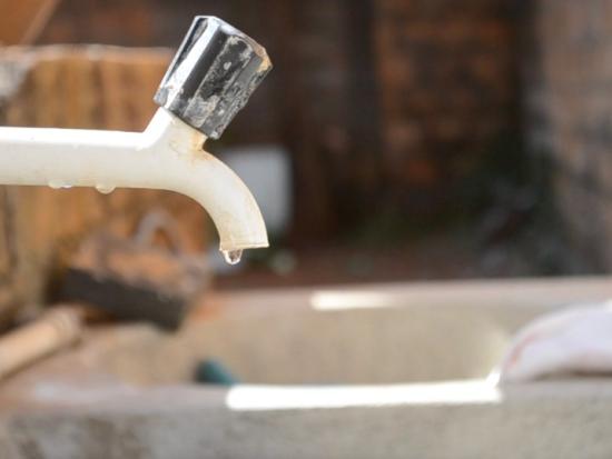 A white faucet with silver knob sits above an outdoor sink as a water droplet gathers from it.