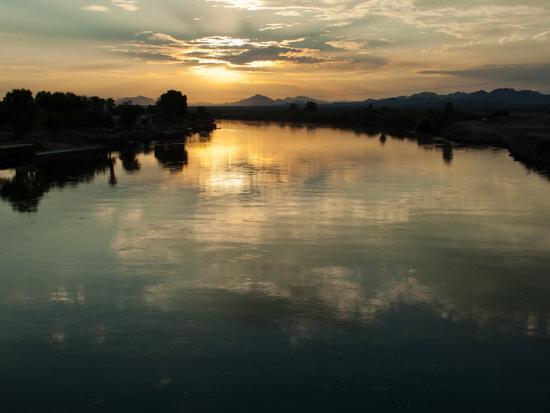 Sun setting over body of water with mountains in the backdrop.