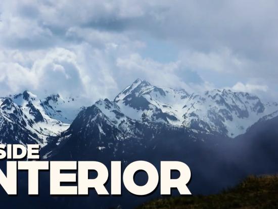 Snow capped mountains are seen under a cloudy blue sky
