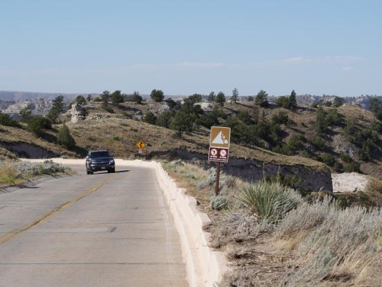 A vehicle drives on a concrete-surfaced road with bluffs in the background.