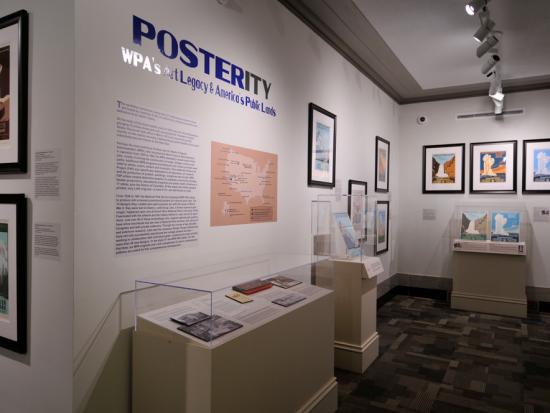 View of a museum exhibition gallery with a title and intro panel with vitrines