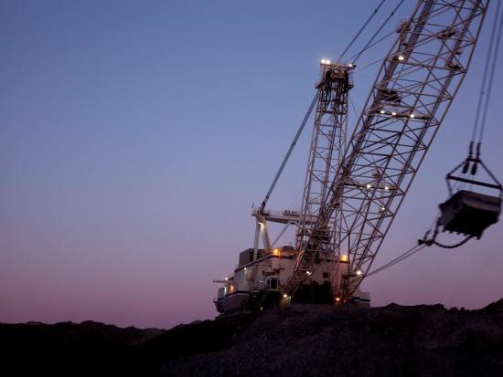 Large machinery on black rocky cliff with pink purple hued sunset.