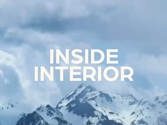 The white text Inside Interior over rocky snow capped mountains blanketed in fog. 