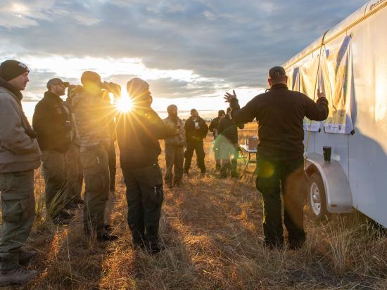 Group of firefighters standing around trailer during morning sunrise meeting.